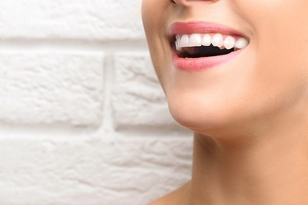The image shows a close-up of a person with a wide smile displaying straight white teeth, against a backdrop of a brick wall.