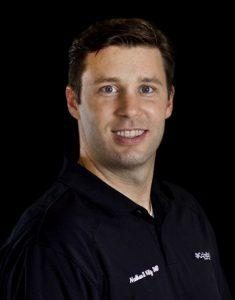 Man wearing a black shirt with a name tag, smiling at the camera.
