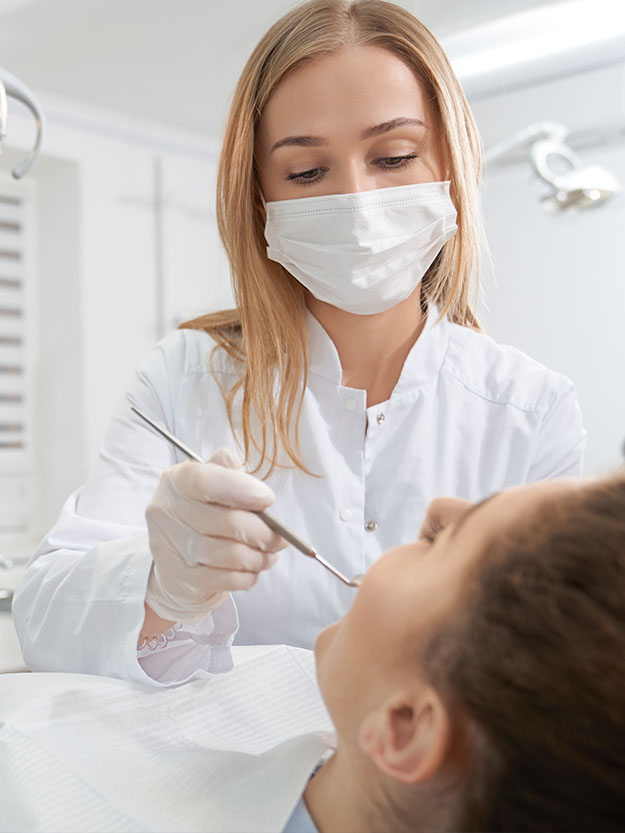 A dental hygienist in a white coat and surgical mask is performing oral care on a patient s teeth using a dental drill, with a focus on precision and cleanliness.
