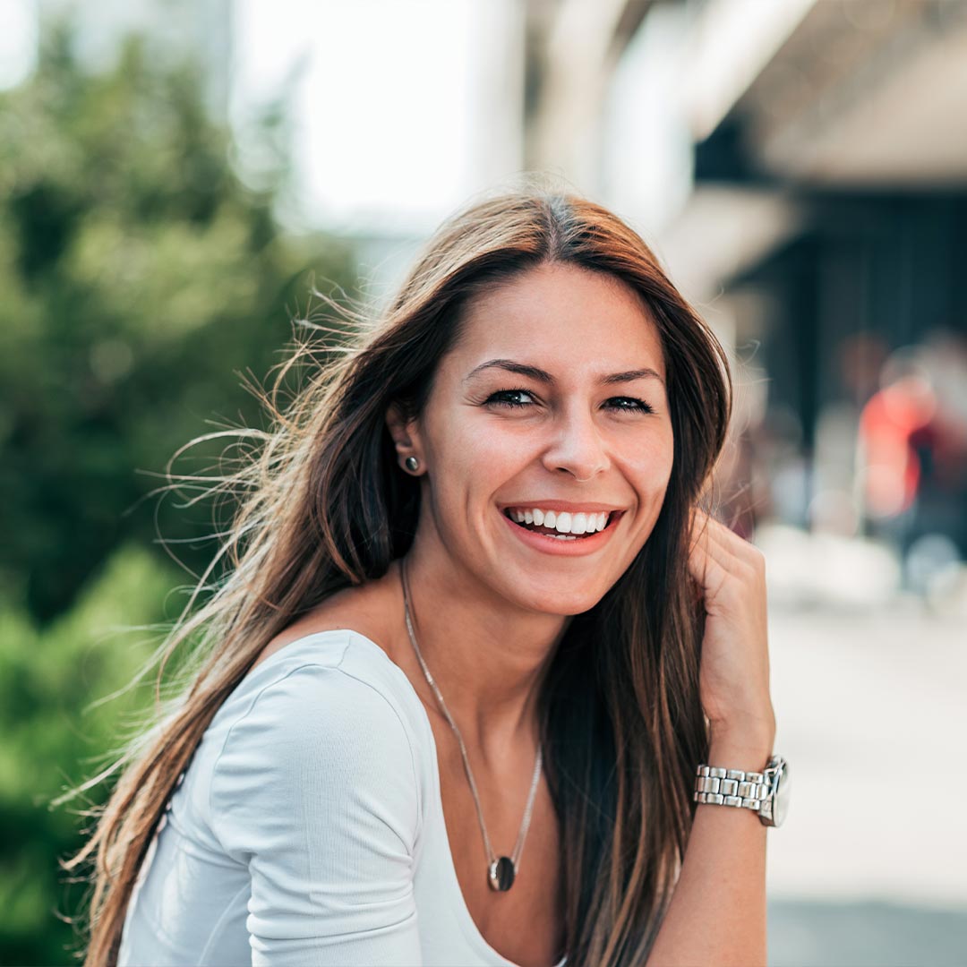 The image features a woman with long hair smiling at the camera while seated outdoors.
