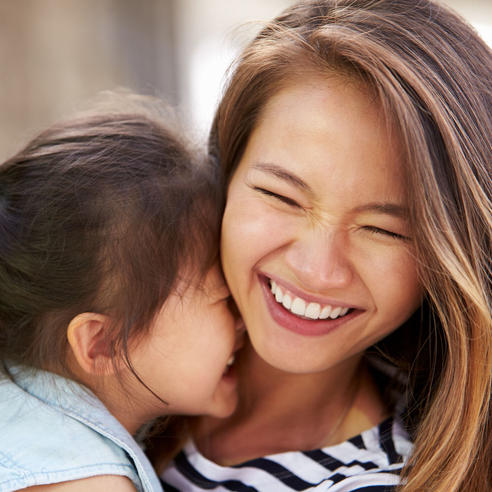 A woman with long hair smiling at a young child who is also smiling.